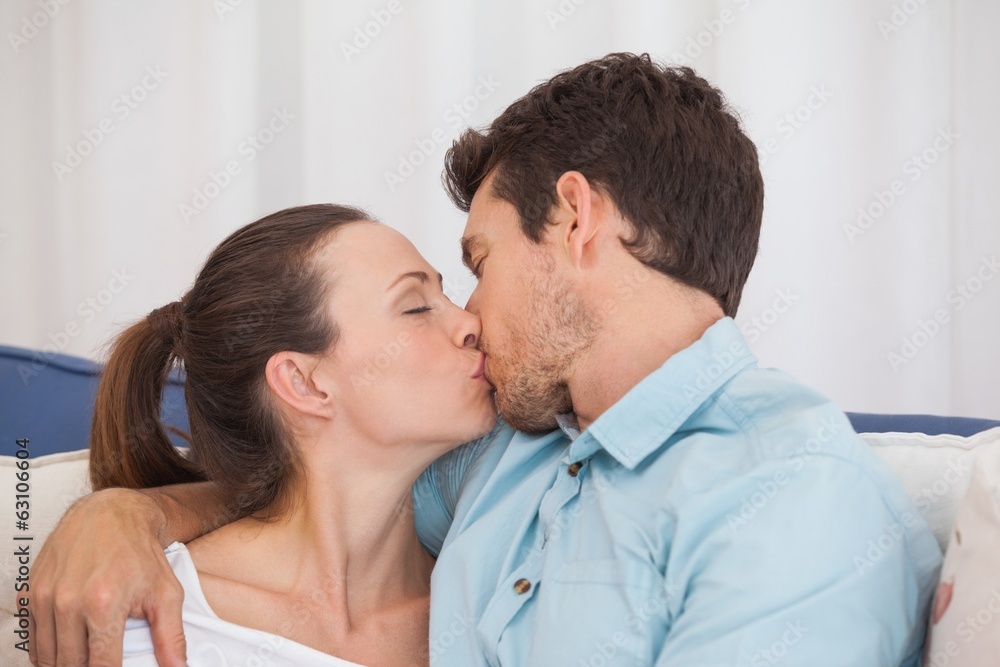Loving young couple kissing on couch Loving young couple kissing on couch