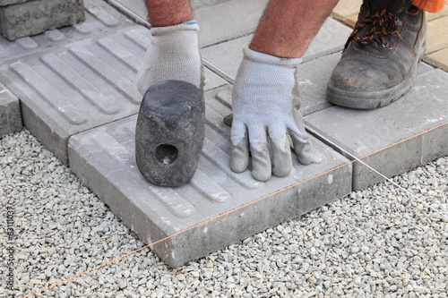 Worker installing concrete brick pavement, using hammer