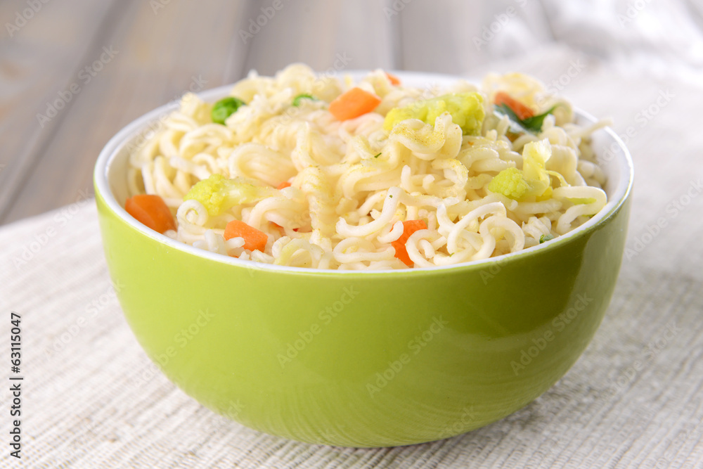 Tasty instant noodles with vegetables in bowl on table close-up Tasty instant noodles with vegetables in bowl on table close-up
