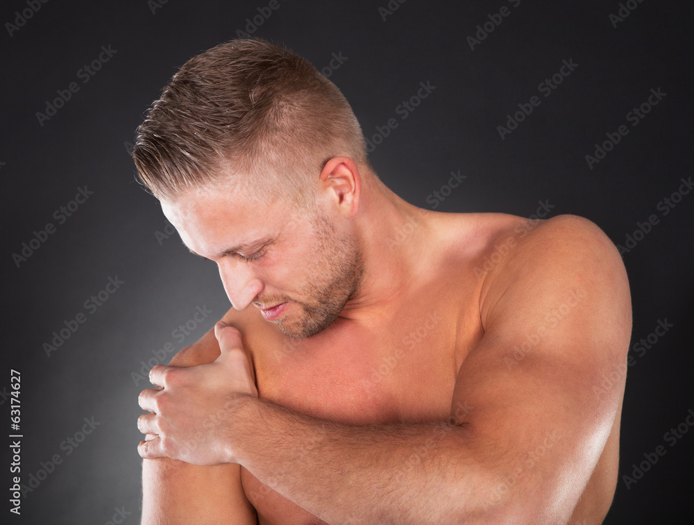 Muscular sportsman massaging his shoulder Muscular sportsman massaging his shoulder