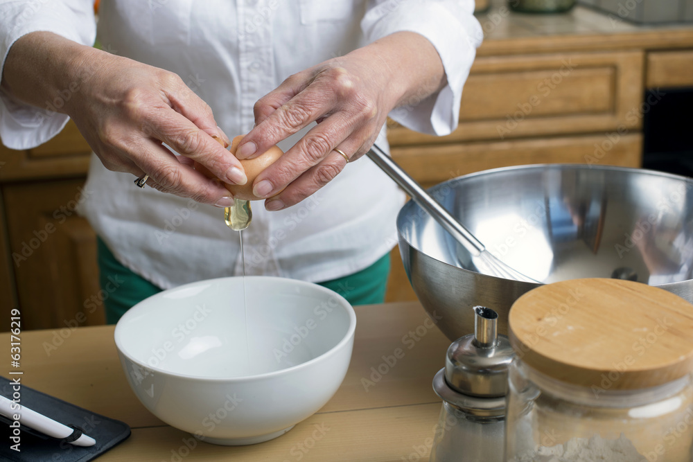 Female hands breaking eggs into a bowl; closeup Female hands breaking eggs into a bowl; closeup