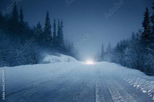 lights of car and winter road in forest