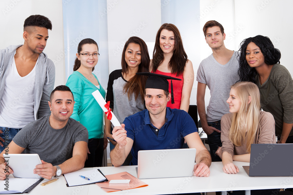 College Student Holding Degree With Classmates Looking At Him College Student Holding Degree With Classmates Looking At Him