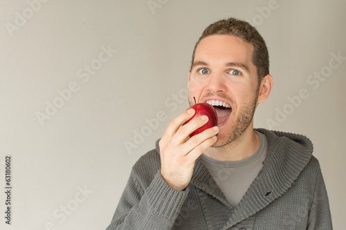 Young man eating an apple over a grey background
