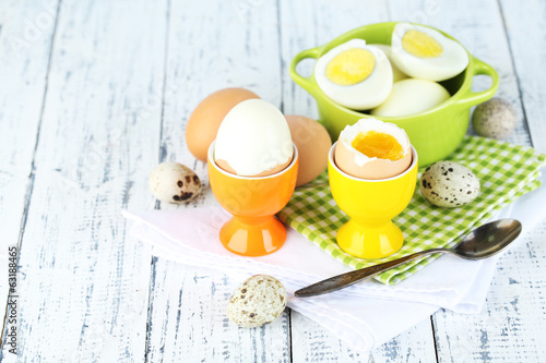 Boiled eggs in pan and eggcup on color wooden background