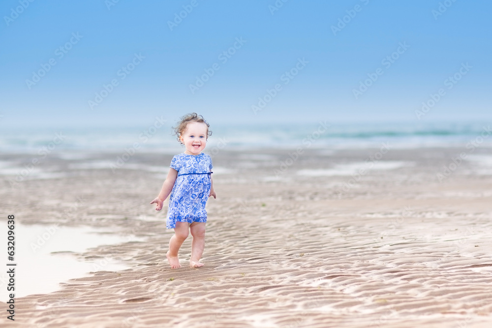Laughing toddler girl in a blue dress running at a beach Laughing toddler girl in a blue dress running at a beach