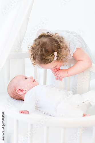 Cute toddler girl in a white dress kissing the hand of her baby