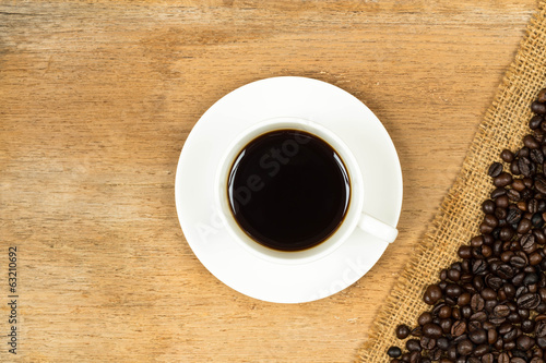 Coffee cup and roasted beans over hessian on wooden table