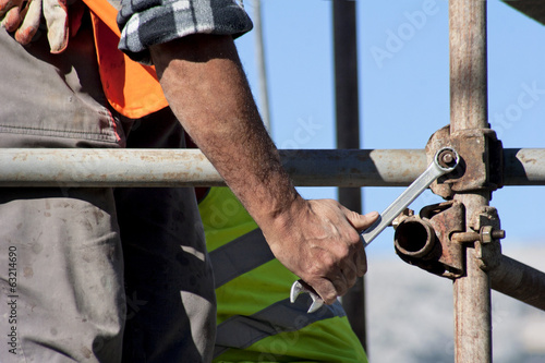Foto Worker with wrench builds scaffolding on construction site