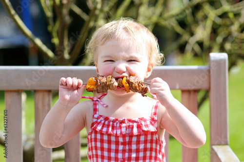 Funny toddler girl eating bbq meat outdoors in the garden