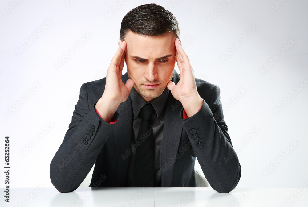Pensive businessman sitting at the table over gray background Pensive businessman sitting at the table over gray background