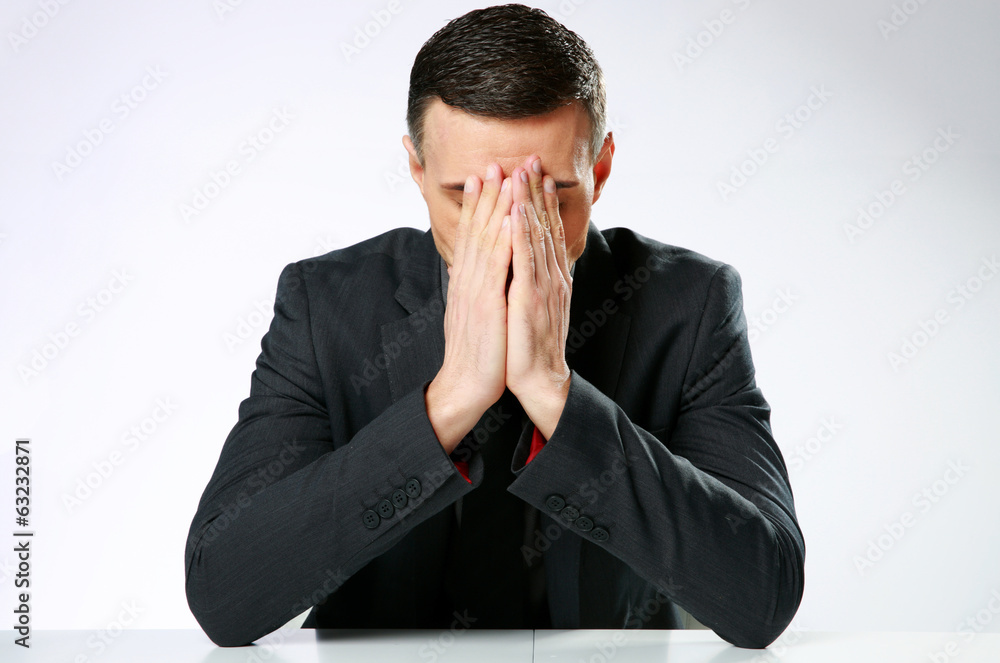 Frustrated businessman sitting at the table with hands on face Frustrated businessman sitting at the table with hands on face
