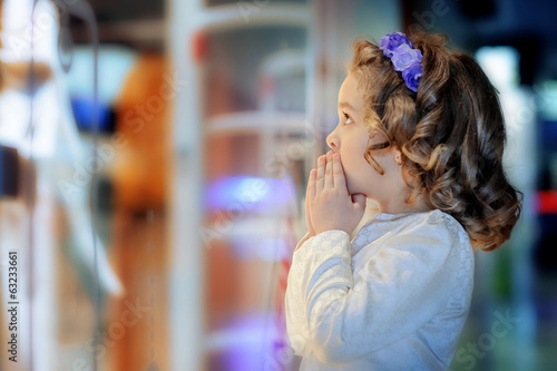 Little cute girl looking at shop window in the mall.