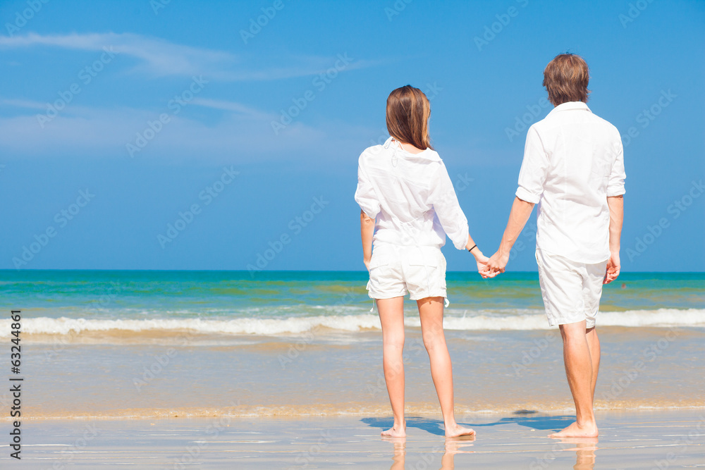 Young happy caucasian couple in white standing on beach looking