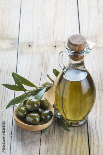 Aceitera y cuchara de palo con aceitunas sobre fondo de madera