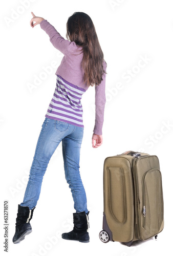 Beautiful young woman traveling with suitcas and pointing at wa