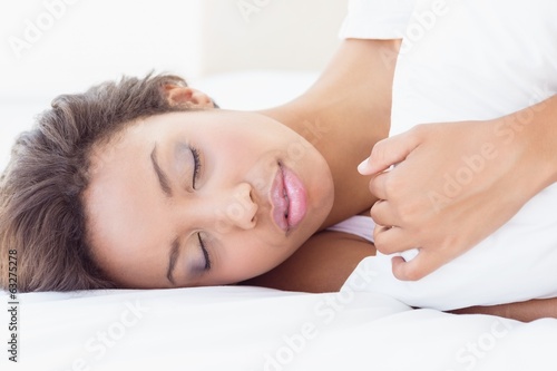 Sleeping pretty brunette lying on bed hugging pillow