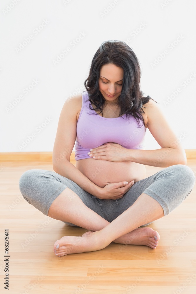 Pregnant woman sitting on floor holding belly Pregnant woman sitting on floor holding belly