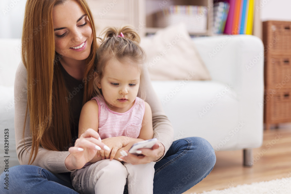 Mother and little girl using mobile phone at home Mother and little girl using mobile phone at home
