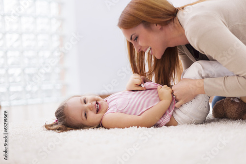 Loving mother tickling her little girl on carpet at home