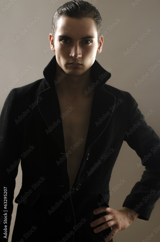 Fototapeta premium Portrait of a beautiful young man dressed in a black long coat