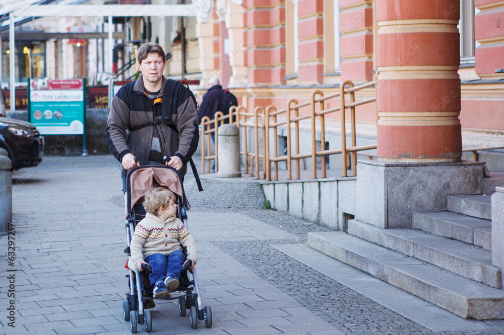 Father walking with little son in stroller in the city