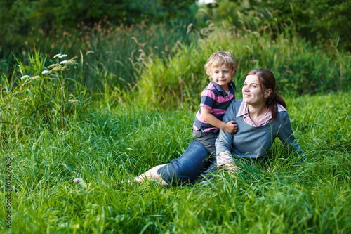 Little boy and his mother sitting on grass in summer forest