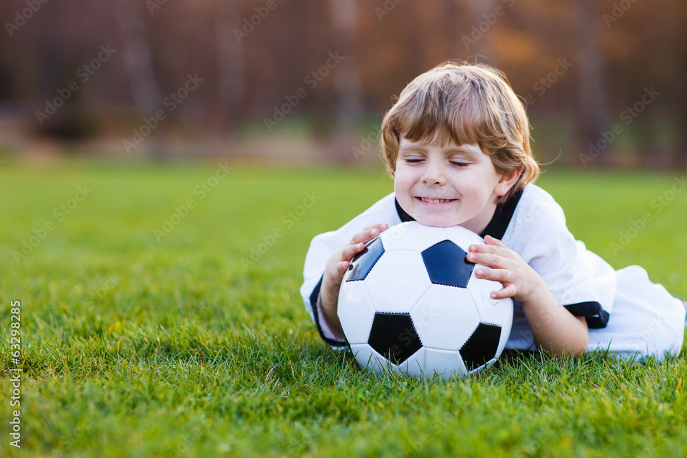 Blond boy of 4 playing soccer with football on football field