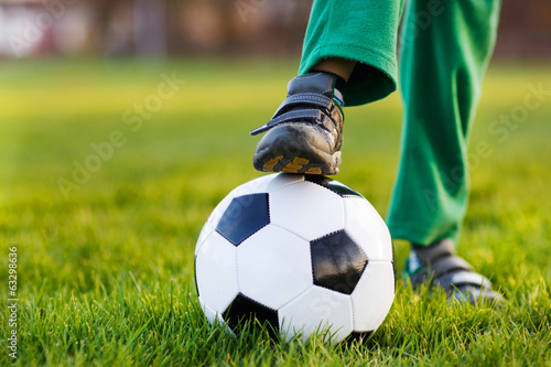Feet of little boy with football on football field, outdoors
