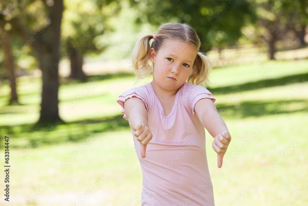 Displeased girl gesturing thumbs down at park Displeased girl gesturing thumbs down at park