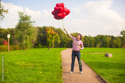 Young happy man with red balloons walking in the park