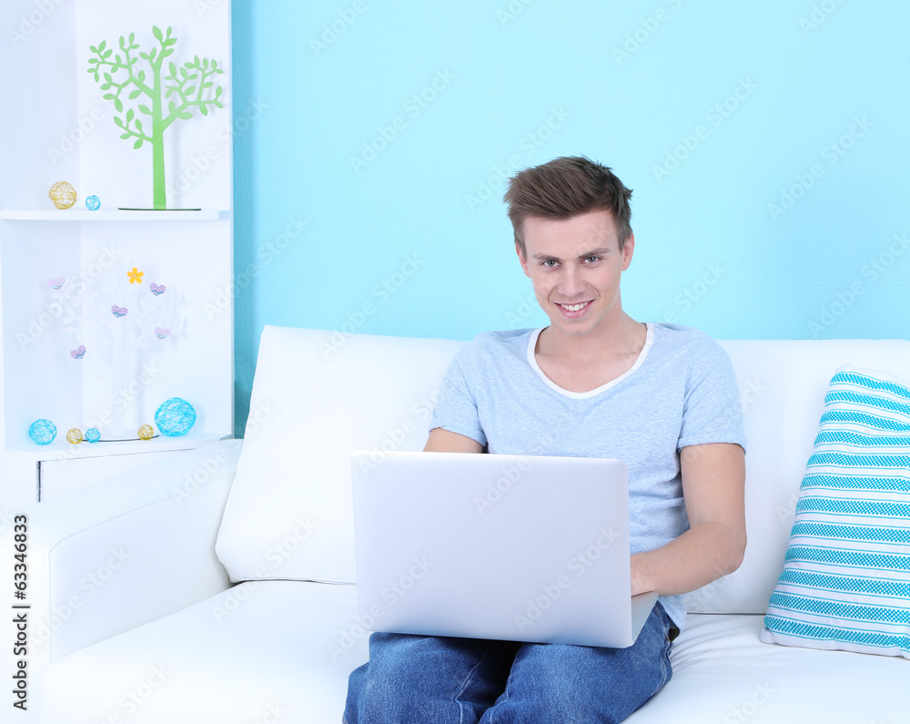 Guy sitting on sofa with laptop on blue background Guy sitting on sofa with laptop on blue background