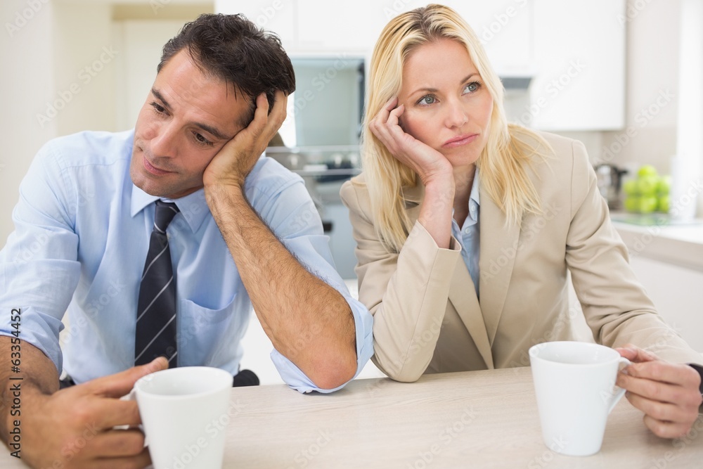 Well dressed thoughtful couple with coffee cups in kitchen Well dressed thoughtful couple with coffee cups in kitchen