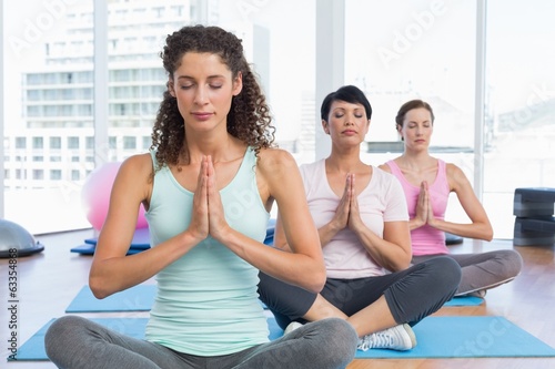 Women with eyes closed and joined hands at fitness studio