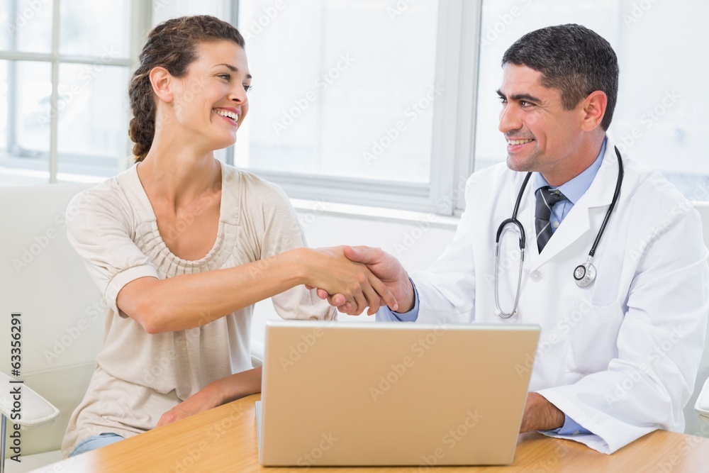 Doctor and patient shaking hands by laptop in office Doctor and patient shaking hands by laptop in office