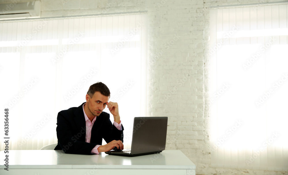 Confident businessman sitting at the table with laptop in office Confident businessman sitting at the table with laptop in office