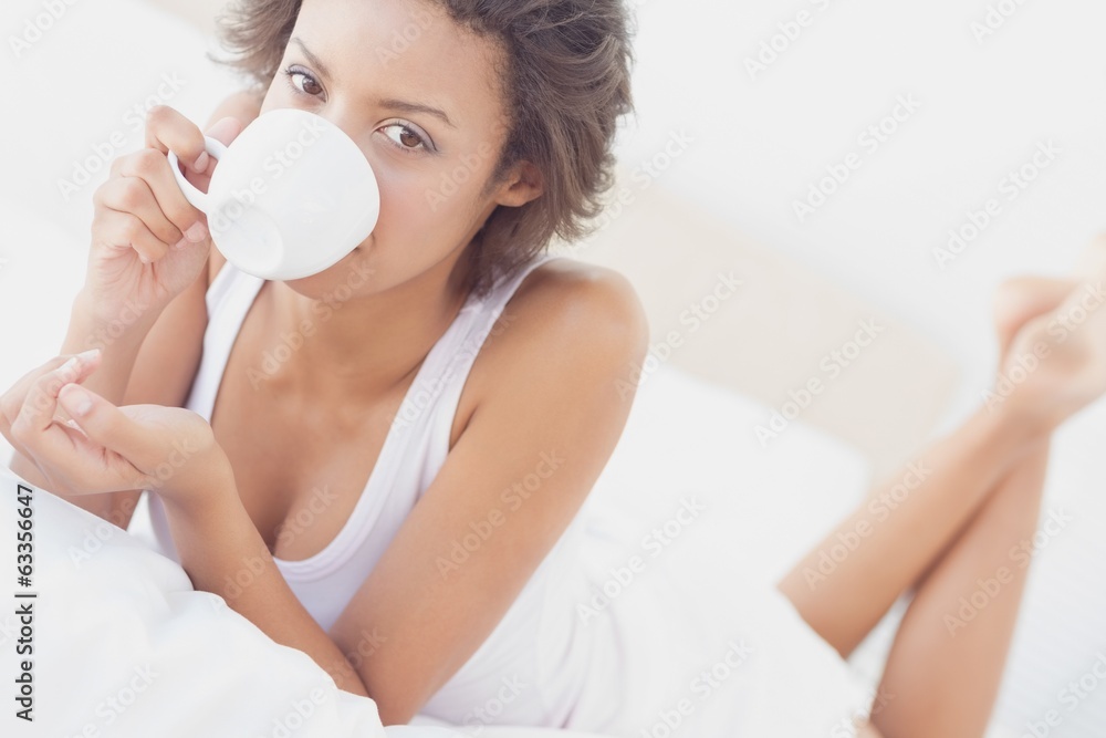 Pretty brunette lying on bed drinking cup of coffee Pretty brunette lying on bed drinking cup of coffee
