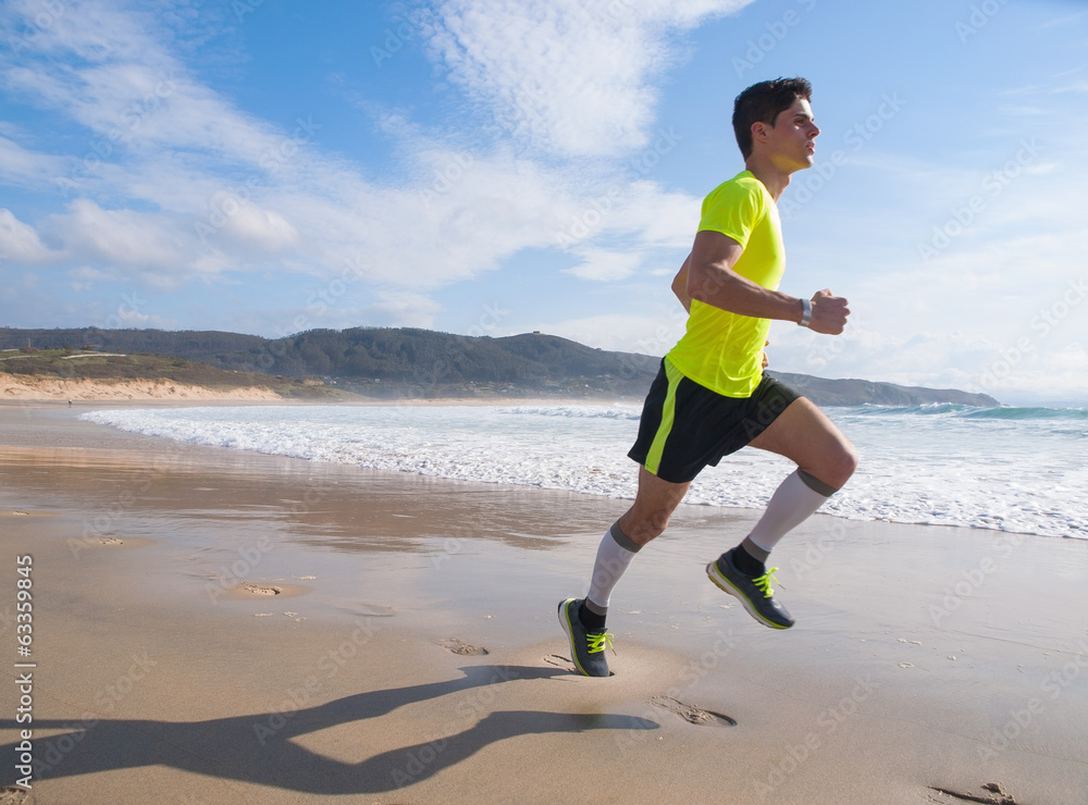 Young Man In Fitness Clothing Running Along Beach Young Man In Fitness Clothing Running Along Beach