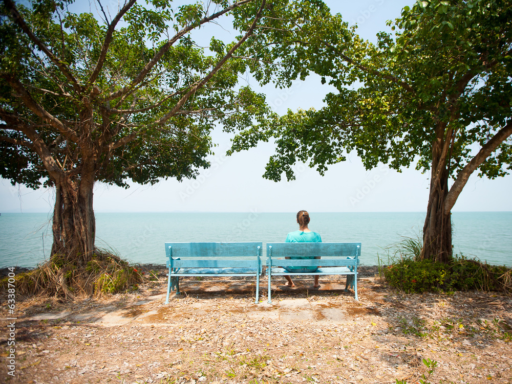 Young man sitting on bench facing the sea Young man sitting on bench facing the sea