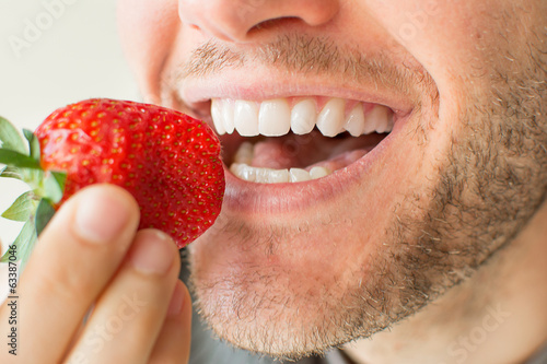 Closeup of man with beard biting a strawberry