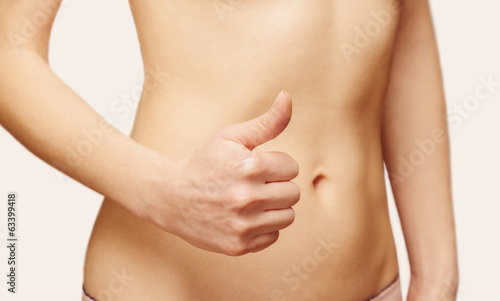 Woman is showing gesture thumb up in front of her abdomen