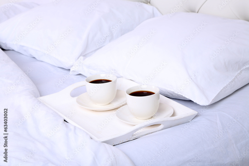 Cups of coffee on comfortable soft bed with pillows