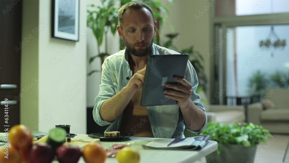 man working on a tablet and eating sandwich at home man working on a tablet and eating sandwich at home