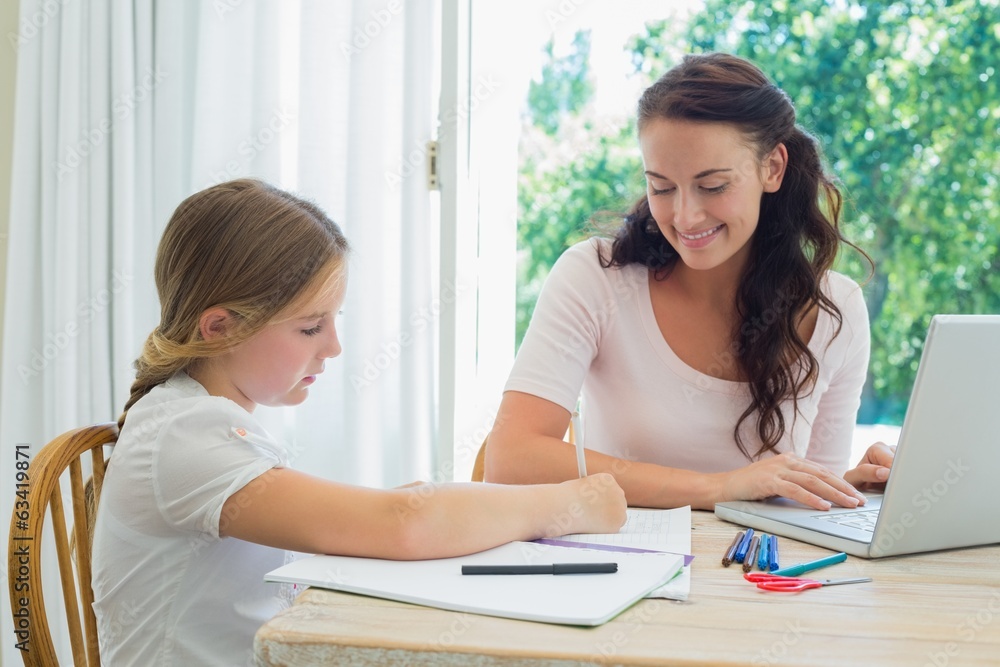 Mother looking at daughter doing homework at table Mother looking at daughter doing homework at table