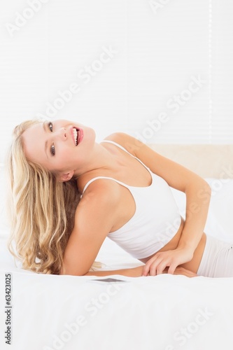 Happy blonde woman lying on bed smiling at camera