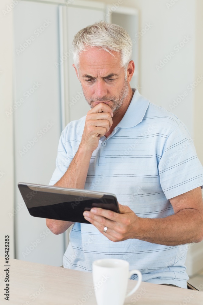 Fototapeta premium Thoughtful man using his tablet at breakfast
