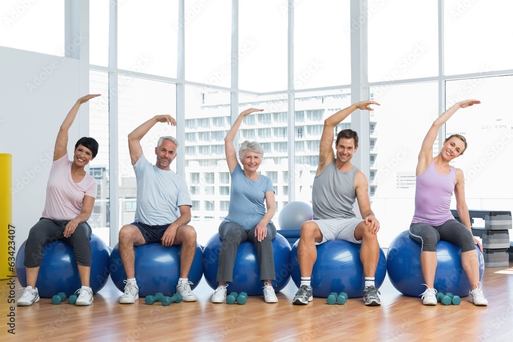 Fototapeta premium Class sitting on exercise balls and stretching hands in gym