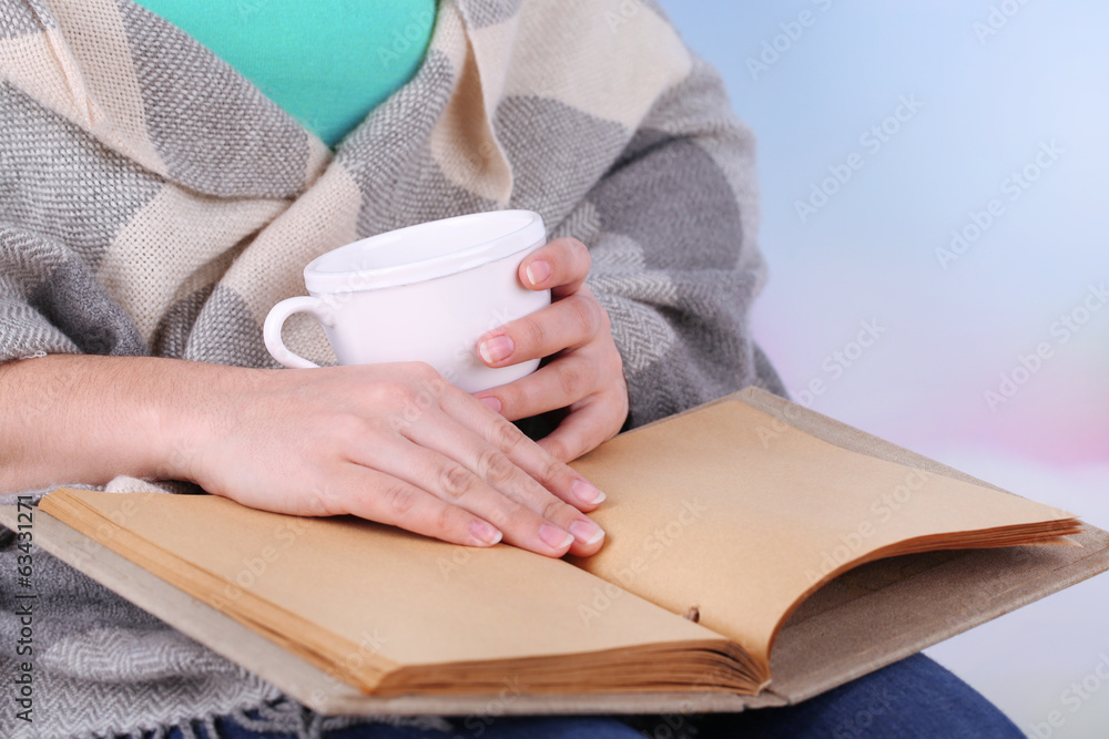Obraz premium Woman reading book and drink coffee or tea, close-up