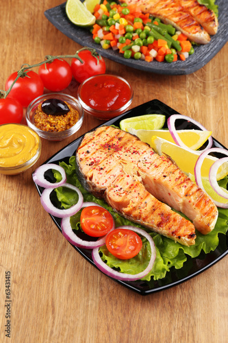 Tasty grilled salmon with lemon and vegetables, on wooden table