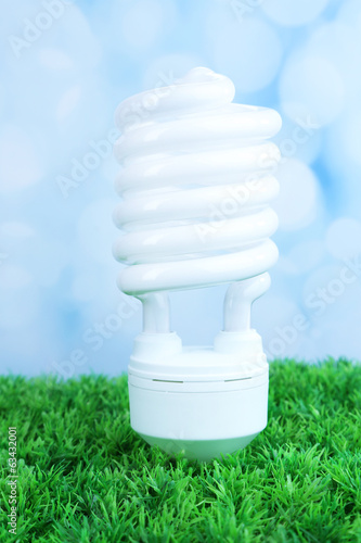 Energy saving light bulb on green grass, on light background